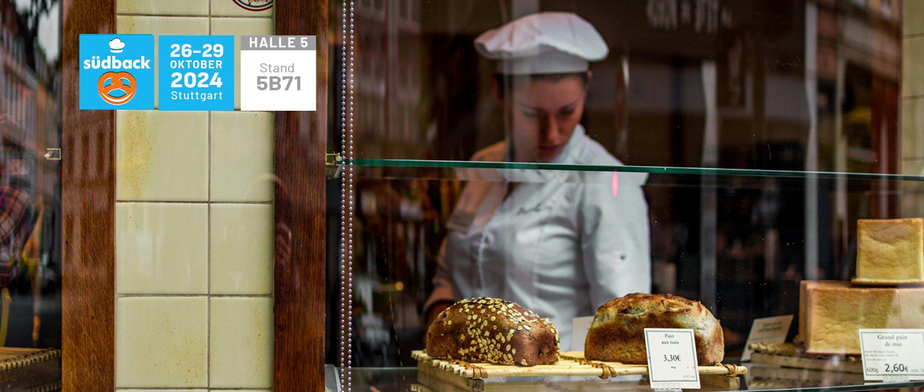 Bäckerin in Bäckerei schaut in Auslage Messeaushang Südback 2024